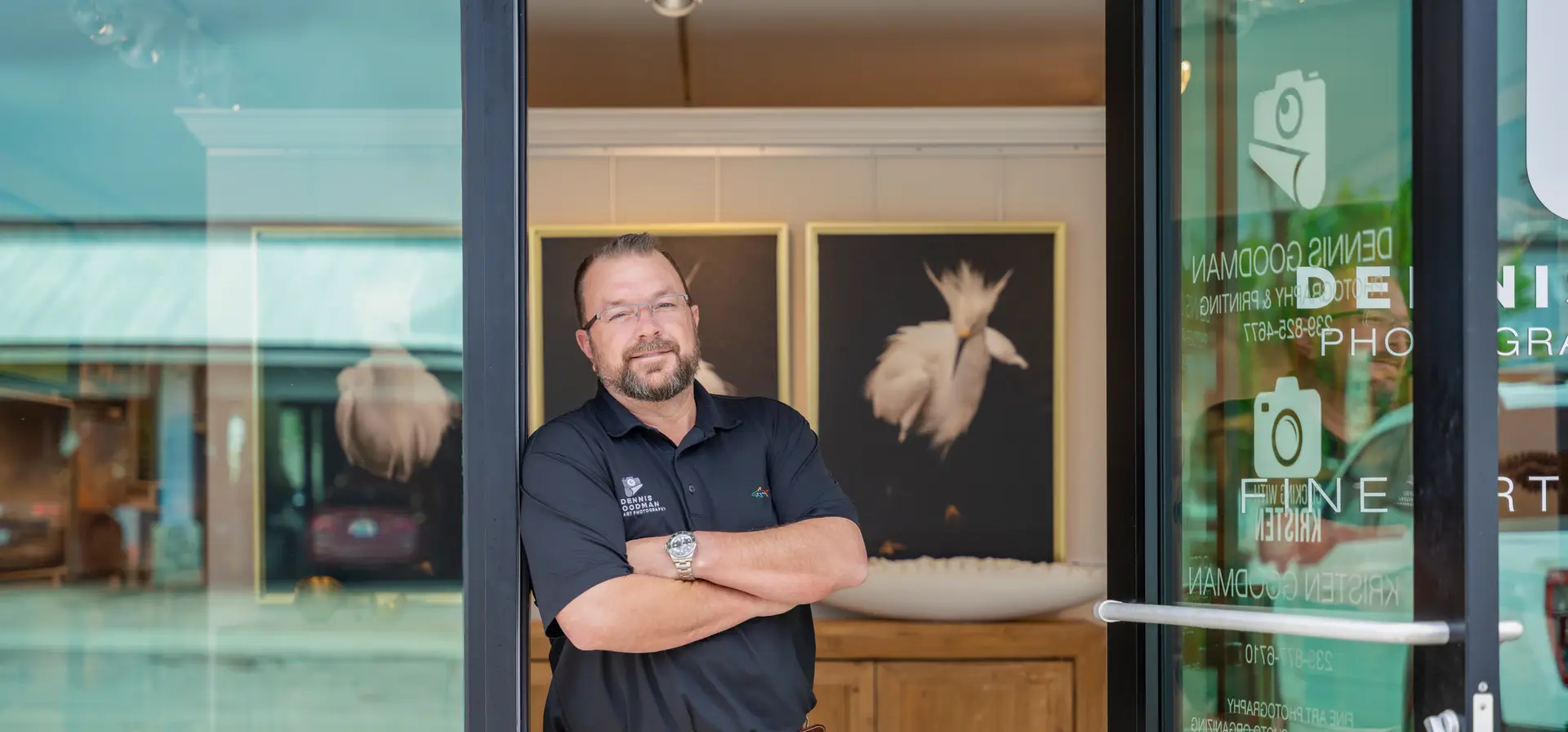 Man standing with arms crossed in front of framed artwork.